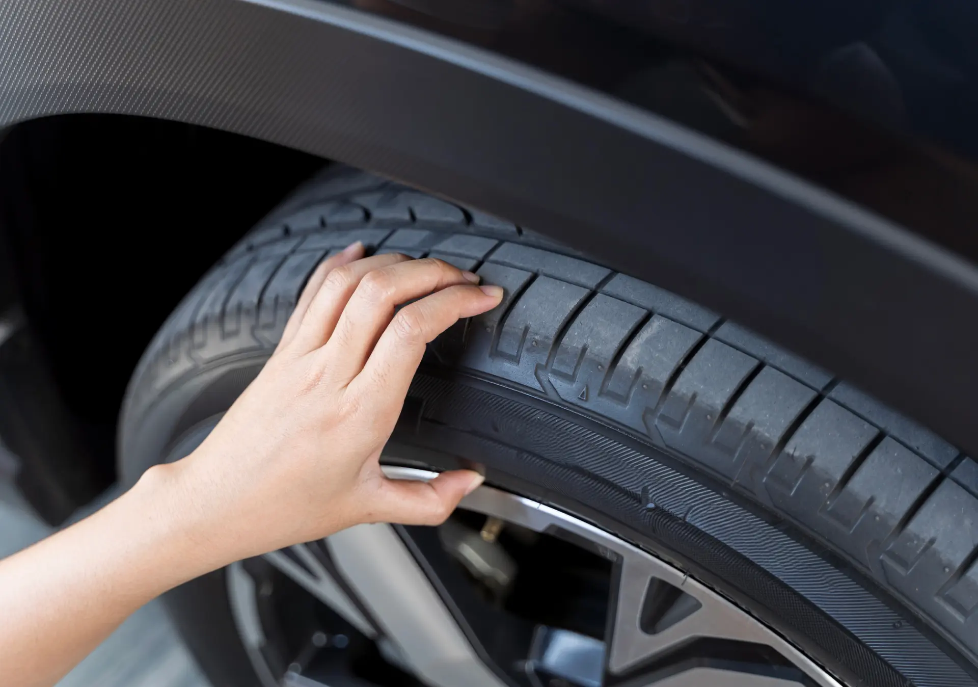 Hand inspecting car tire tread depth.